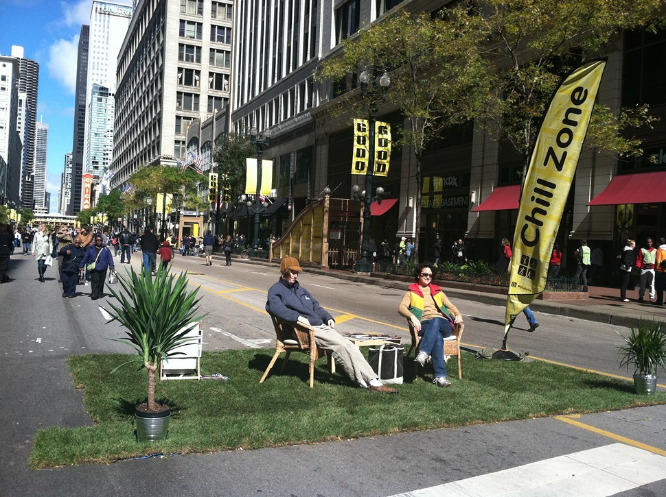 People sit in a the middle of the street with temporary grass turf.