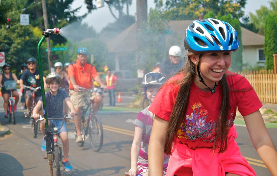 People ride bikes through a mister.