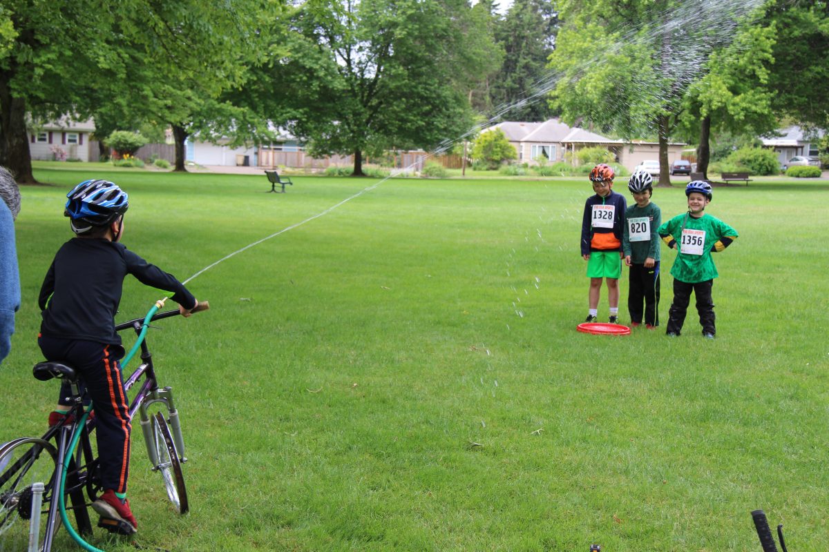 Kids get sprayed by water hose attached to bicycle.