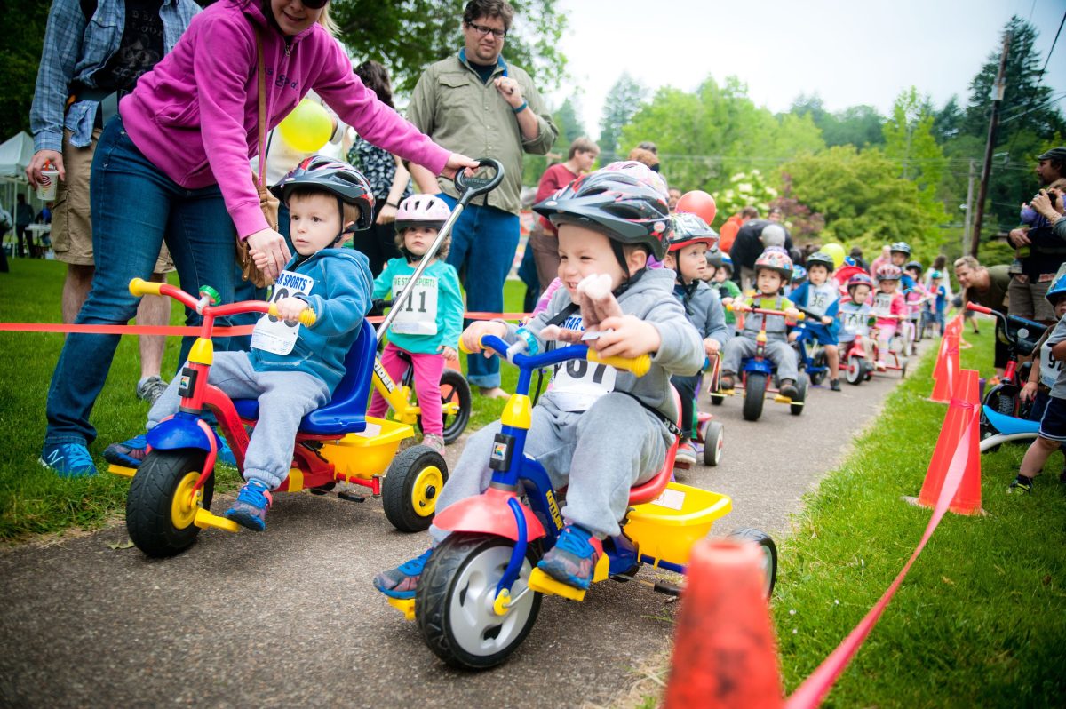 Toddlers ride trikes down the sidewalk.