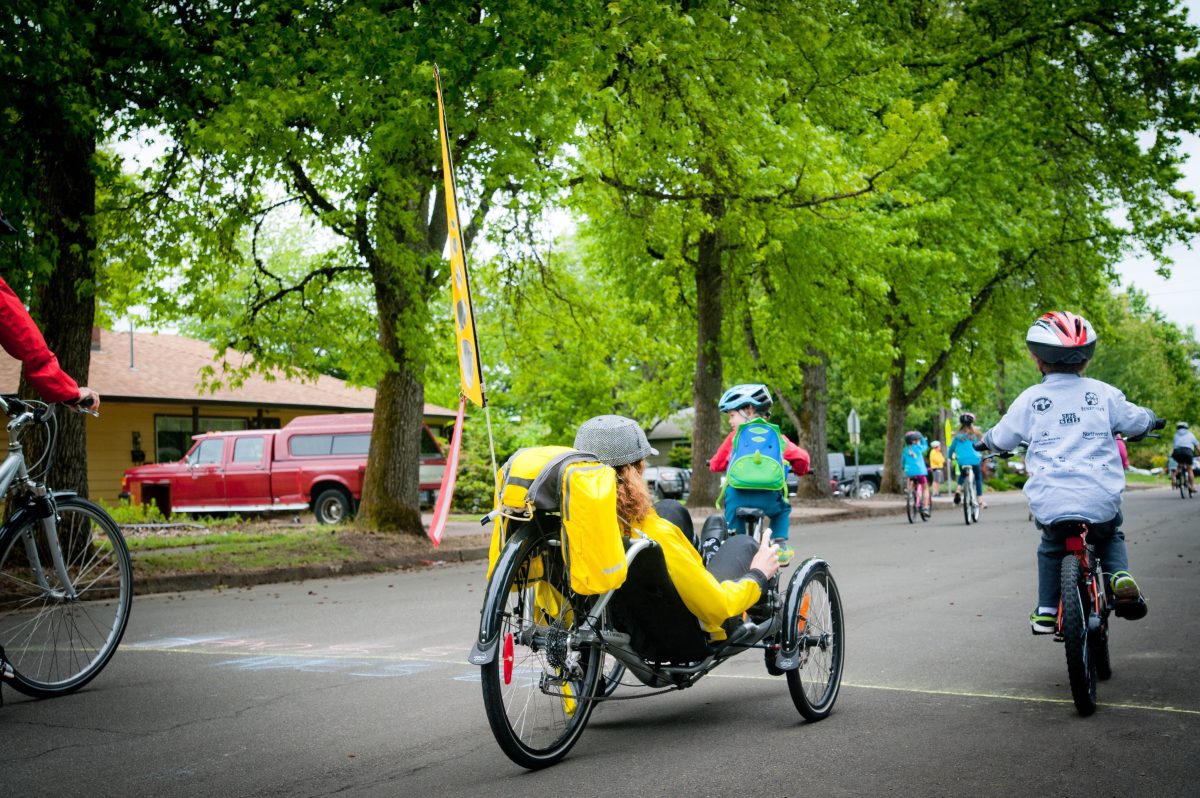 A person rides a recumbent bike alongside some kids on bikes.