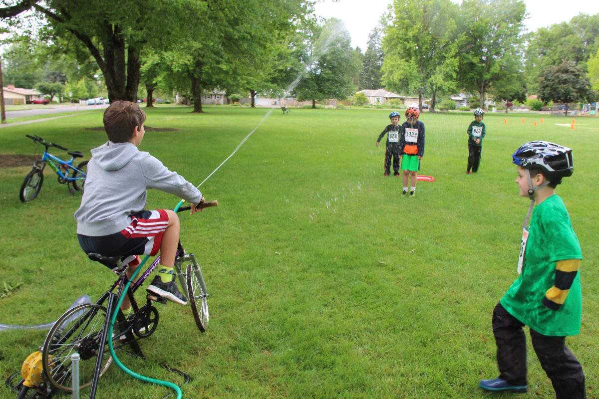 Kids get sprayed by water hose attached to bicycle.