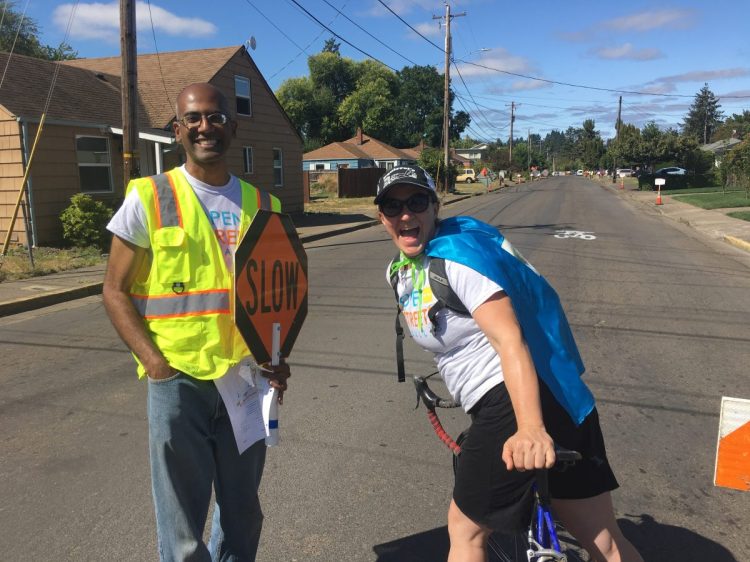 Two volunteers on the street, one holding a slow sign and the other wearing a cape.