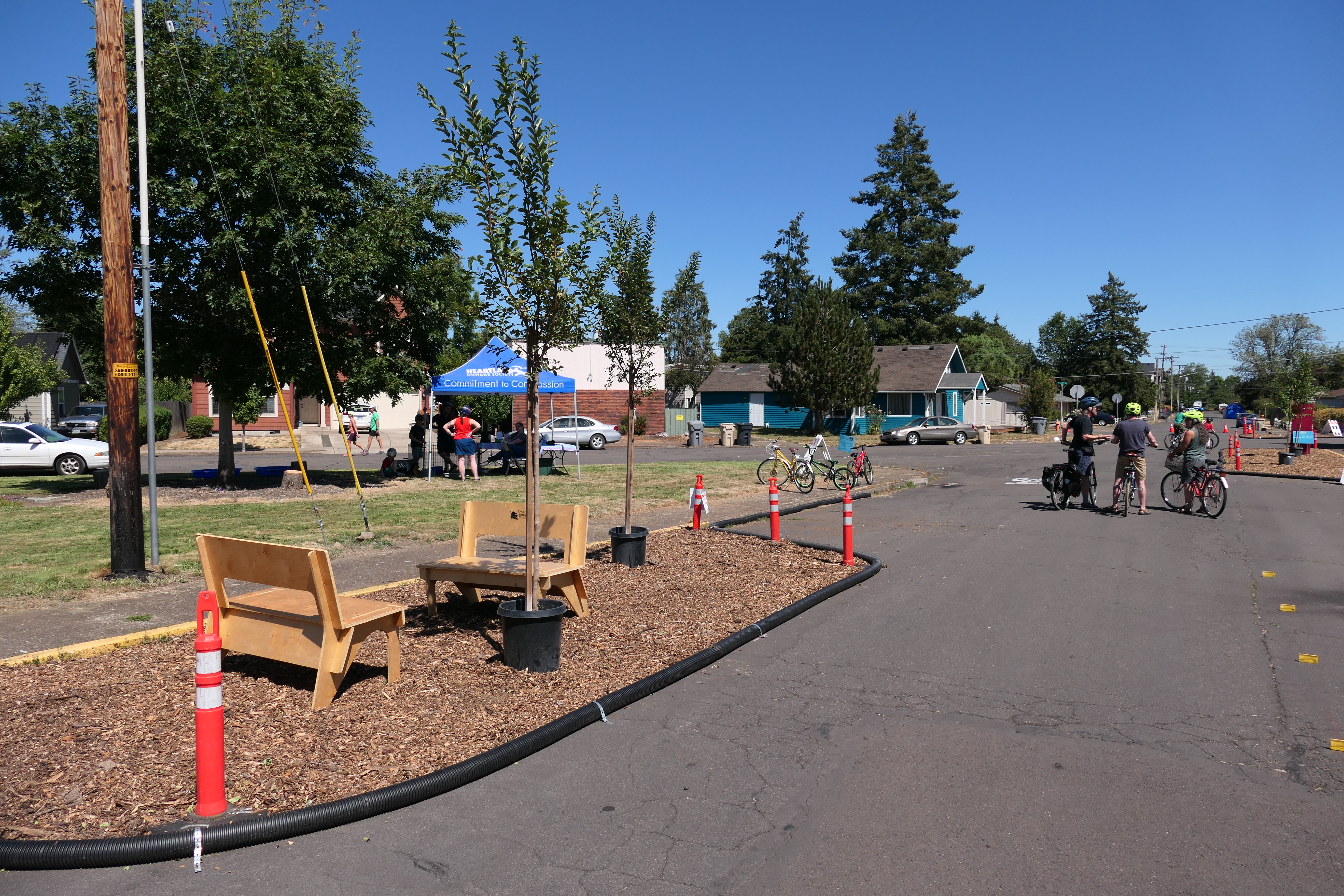 A few cyclists stop in the middle of the street near a temporary curb extension with benches and potted trees.