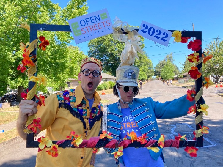 Two people dressed in colorful costumes pose in a frame labeled Open Streets 2022.