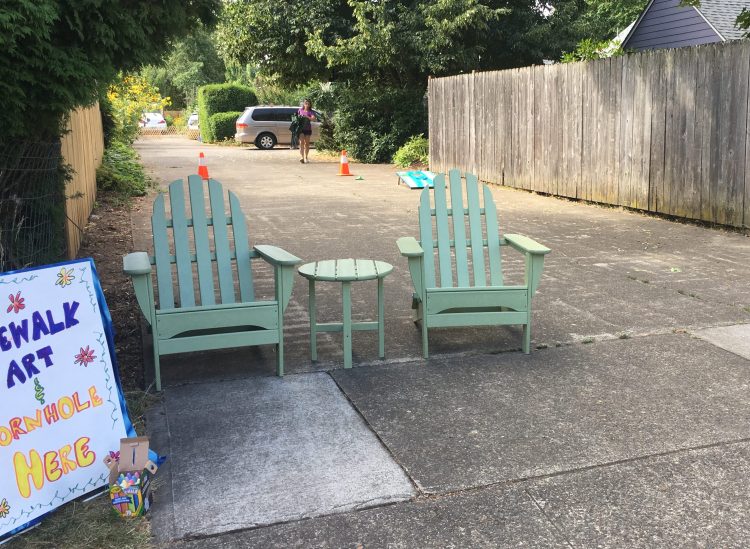 Two wooden lounge chairs and a small table are set up in a driveway