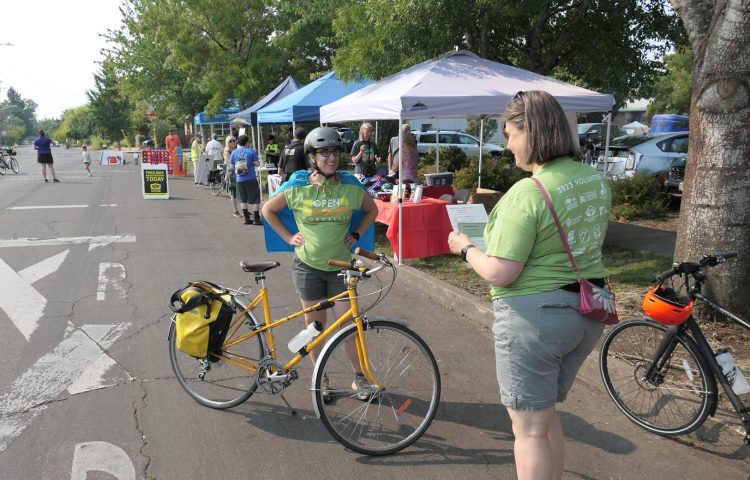 A volunteer holding a piece of paper talks to another volunteer standing by a bike.